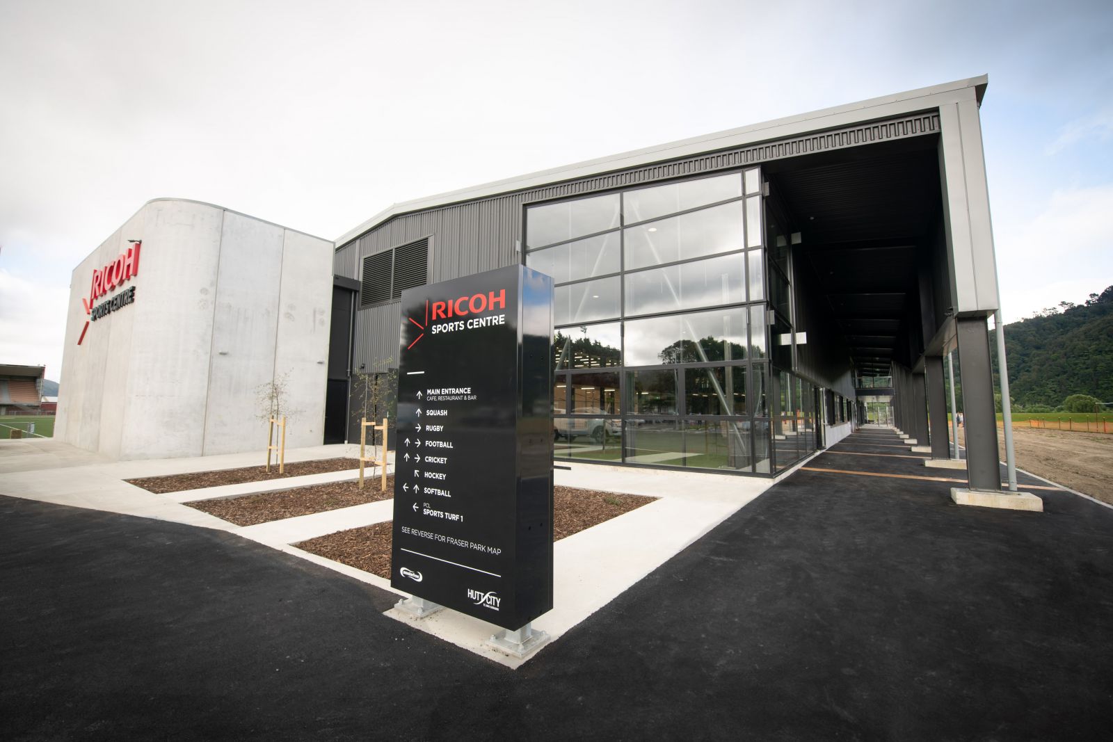 Shows the entrance as you approach the Ricoh Sports Centre with a large directional sign pointing to where to go for a range of sports. banner image